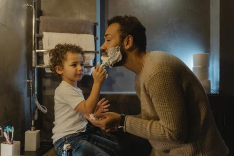 Child helps father apply shaving cream.